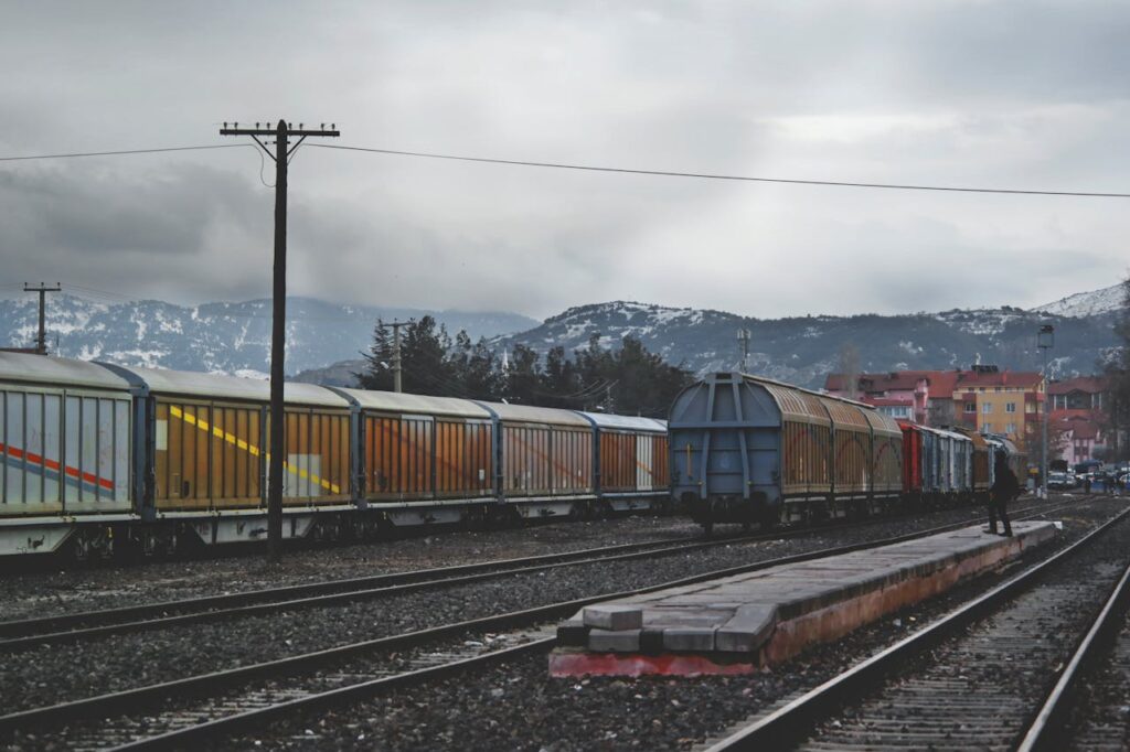 A freight train with colorful cargo wagons on a mountain railway track under a gray sky.
