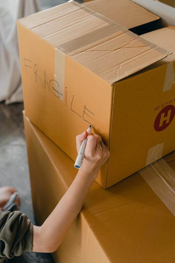 A person writes 'fragile' on a cardboard box using a marker while preparing for a move.